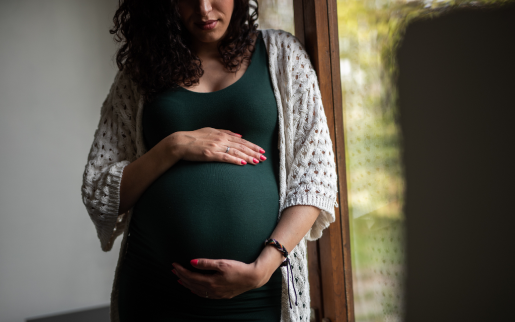pregnant person in front of a window embracing her belly